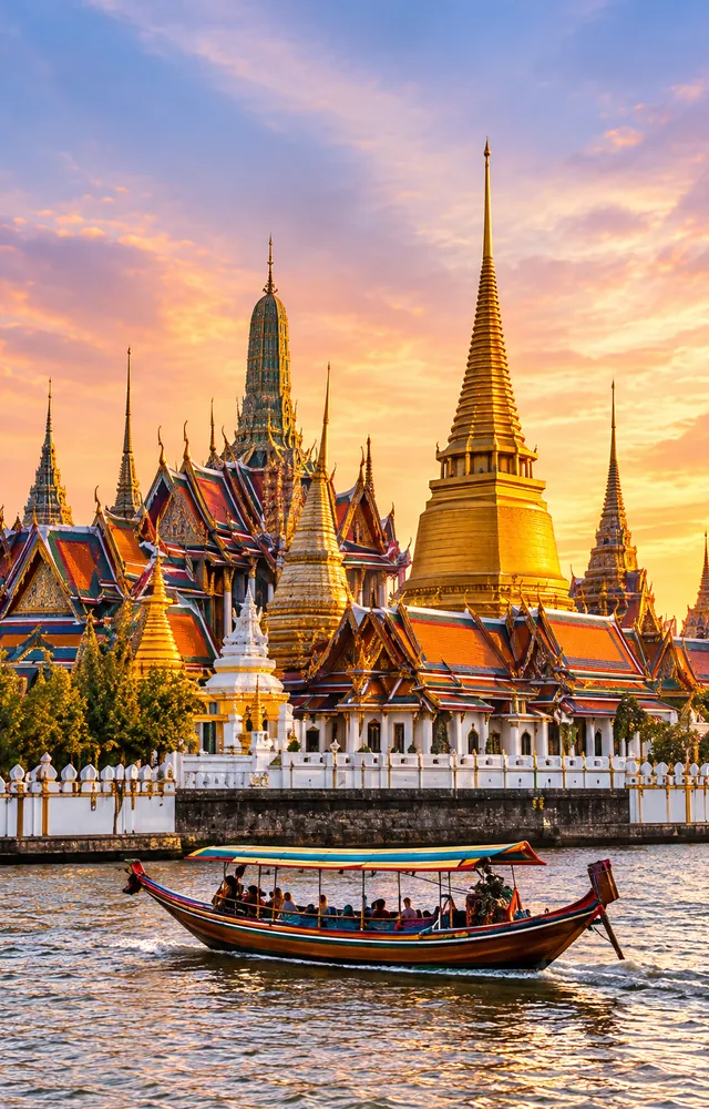 Ornate riverside temple and boats in Thailand at sunset